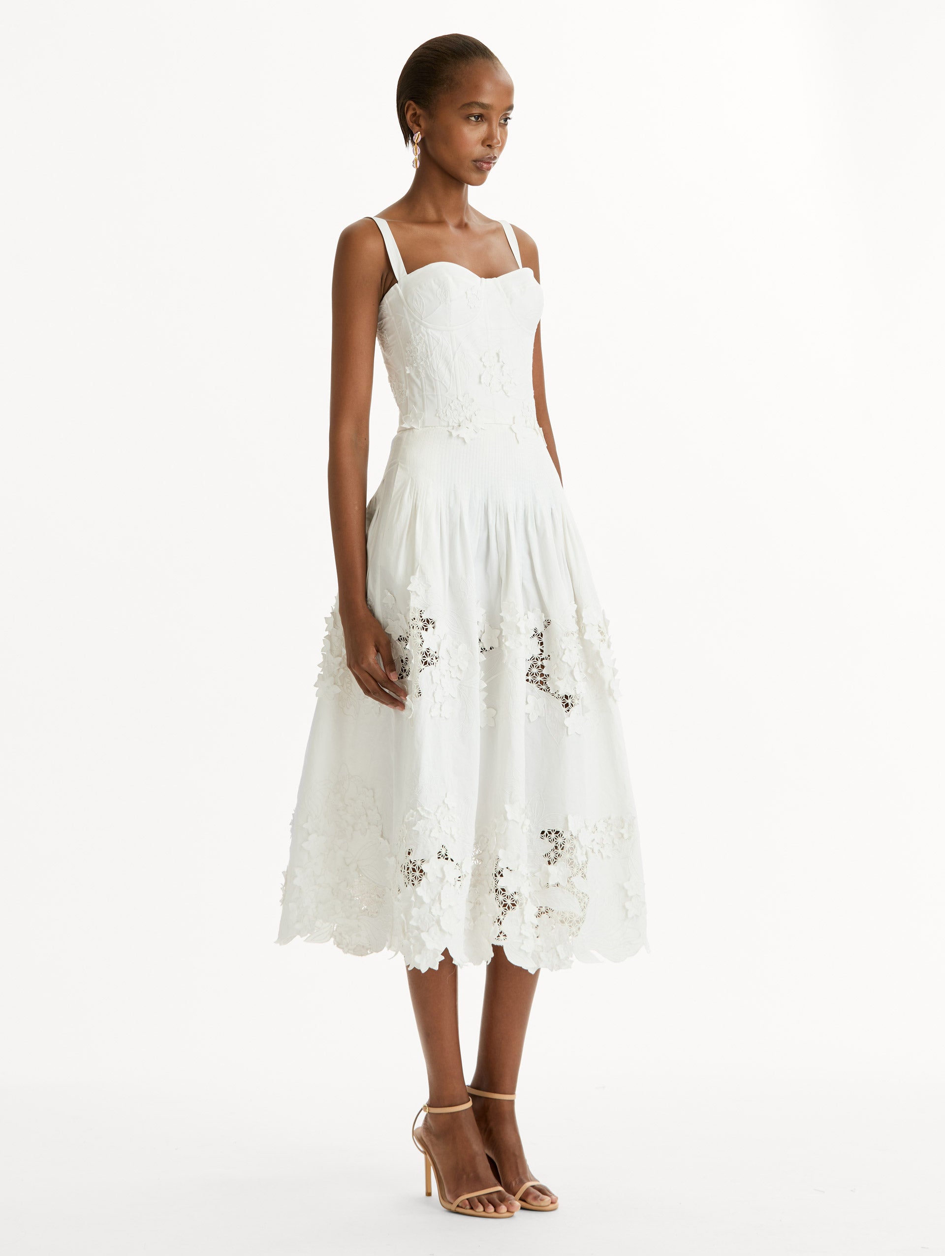 Cotton stretch twill dress. Sculpted bustier bodice with full, midi-length skirt.  porcelain-flower guipure lace along hem. Three-dimensional floral appliqués in layered white-on-white texture. Side View.