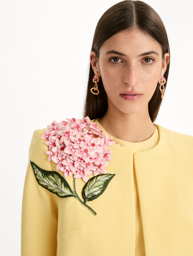 Cropped yellow jacket tailored from double-faced stretch wool and finished with sculptural porcelain flower embroidery at the shoulder. Front View, Close Up.