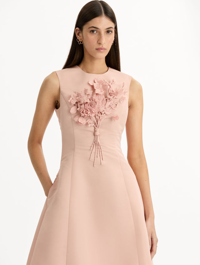Blush pink cocktail midi dress. Centered, three dimensional hand-embroidered bouquet creating the illusion of a bouquet held close to the heart. Halter neck with flared skirt. Front View. 