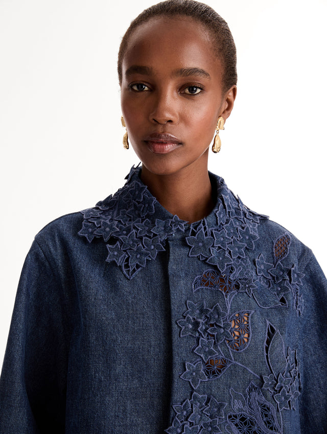 Cropped denim jacket with intricate porcelain flower threadwork and cutout detailing across the front and collar. Long sleeve. Front View, Close Up.
