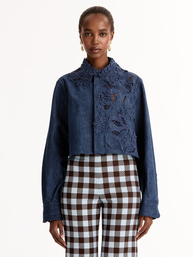Cropped denim jacket with intricate porcelain flower threadwork and cutout detailing across the front and collar. Long sleeve. Front View.