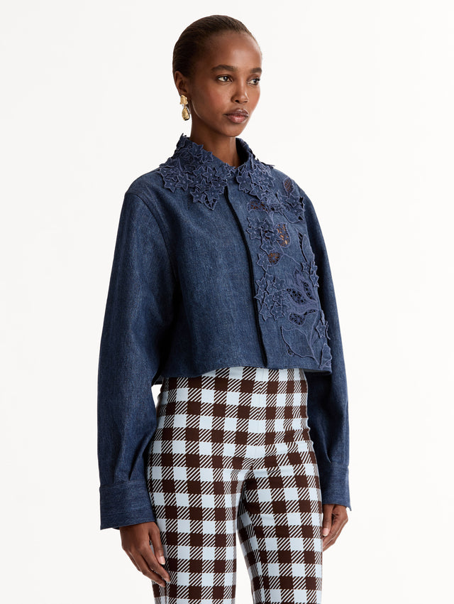 Cropped denim jacket with intricate porcelain flower threadwork and cutout detailing across the front and collar. Long sleeve. Side View.