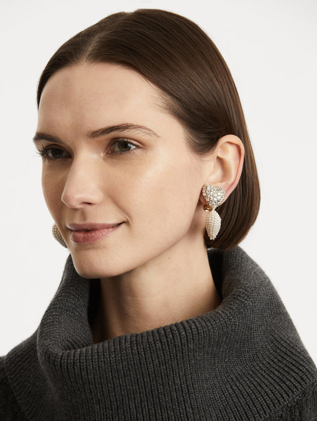 Model is wearing earrings with crystal-encrusted heart anchors which drop to a second heart beaded in lustrous pearls. 