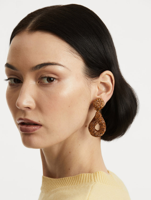 Model is wearing hand-beaded earrings which feature jet-black bugle beads in a bold, open-loop silhouette.