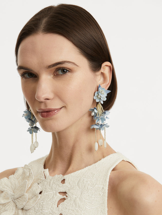 Model is wearing tonal blue petals which form a soft gradient in floral drop earrings, accented with delicate beaded fringe. Finished with white drops.