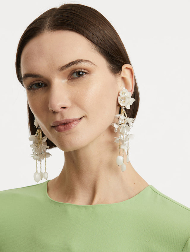 Model is wearing tonal petal earrings which form a soft gradient in these floral drop earrings, accented with delicate beaded fringe. Finished with white drops.