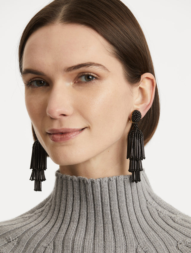 Model is wearing tiered tassel earrings which are crafted from black beads arranged in cascading columns.