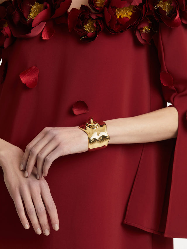 Model is wearing a sculptural gold cuff which features a twisted abstract interpretation of the Oscar “O” emblem with an undulating curve and polished finish.