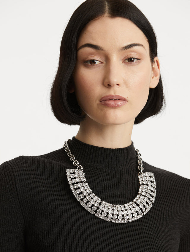 Model is wearing a necklace with a fan of crystals, arranged in structured rows that create a sculptural silhouette. Anchored by a bold chain.