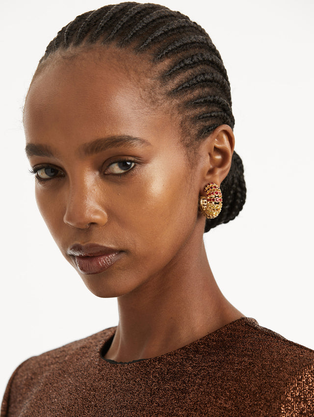 Model is wearing hoop earrings that feature arched rows of faceted crystals in a polished gold-tone setting. 