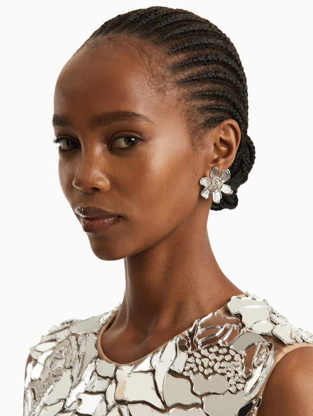 Model is wearing floral post back silver earrings with sculpted petals with the Oscar 'O' and a braided emblem at the center. 