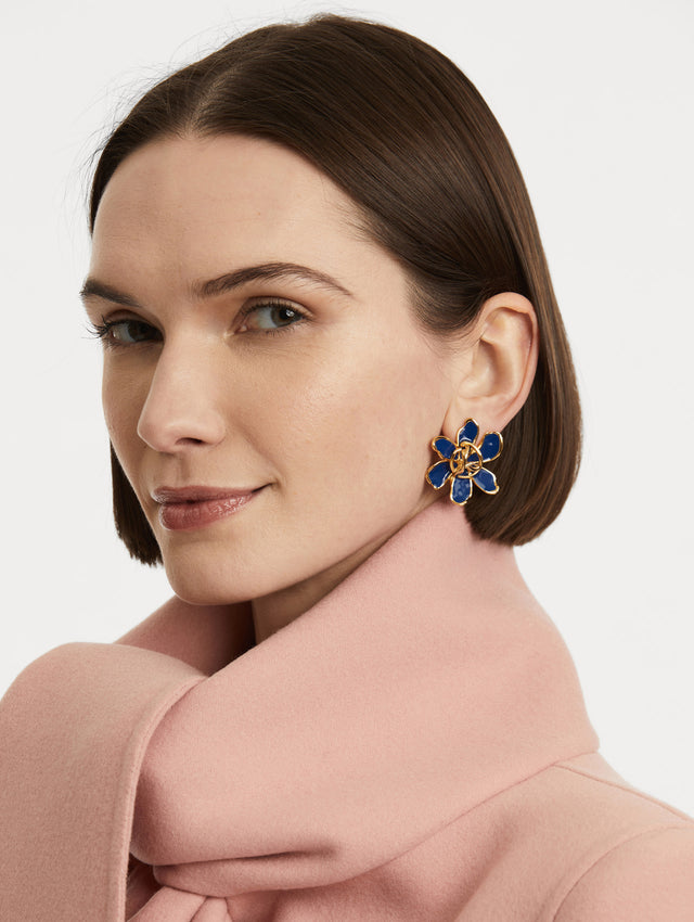 Model is wearing enamel floral earrings with navy sculpted petals that echo the curves of the Oscar 'O' and a braided emblem at the center.