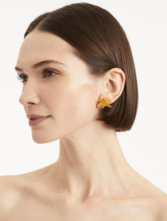 Model wearing gold floral post back earrings with braided oscar o in the center of the flower. 