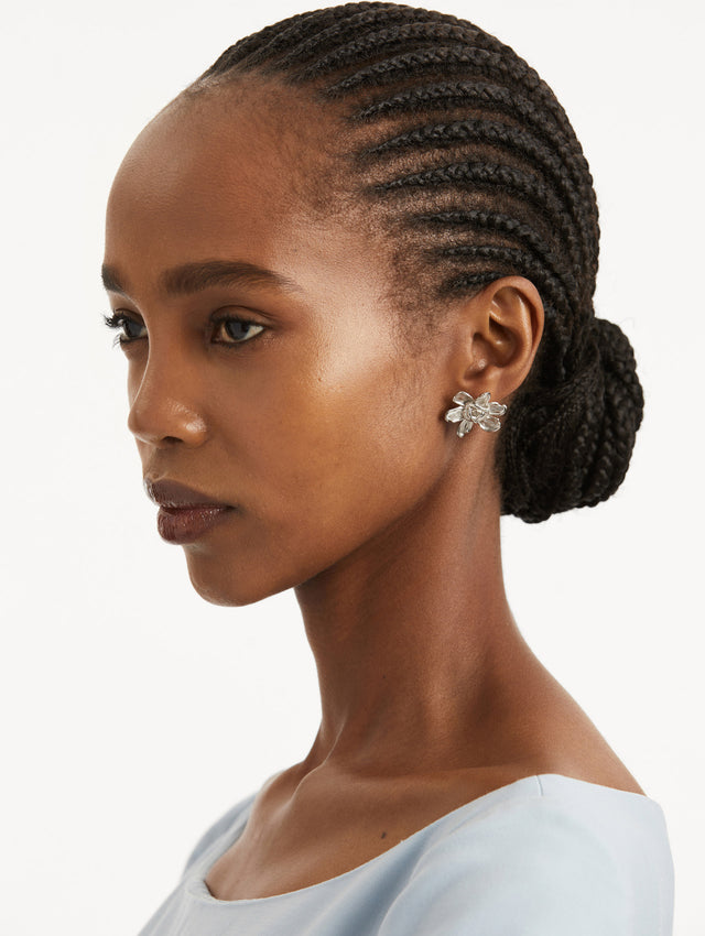 Model wearing silver floral post back earring with braided oscar o in the center of the flower.