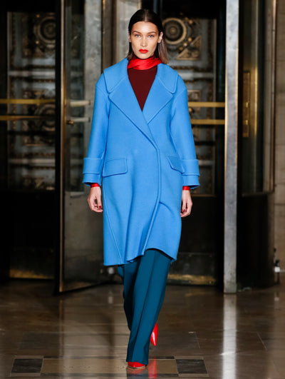 A model wears a blue coat with dark blue pants a burgundy top and a red scarf