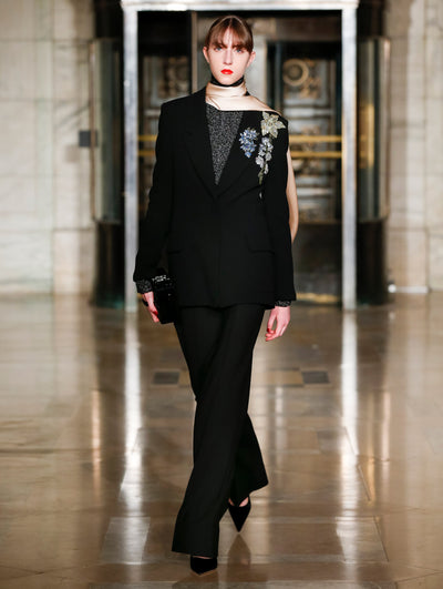 A model wears a black velvet suit set and cream scarf