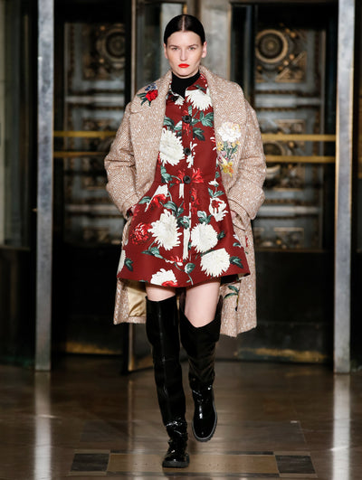A model wears a striped coat and dark orange dress with printed flowers