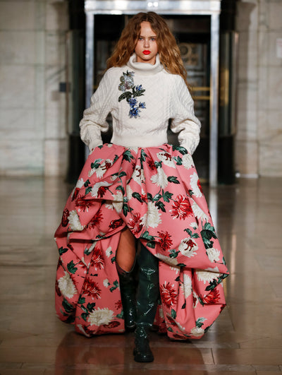 A model wears a high low pink skirt with printed flowers and grey cardigan with an embroidered flower