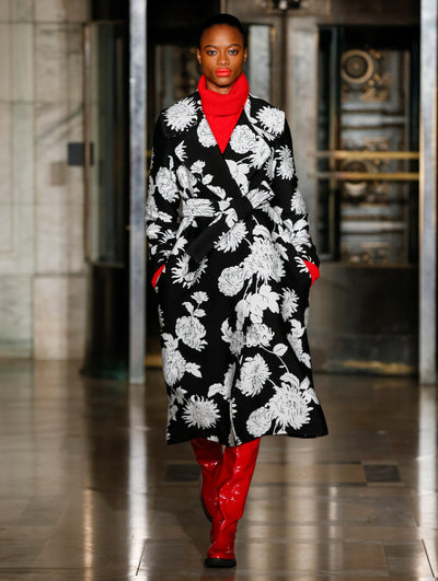 A model wears a black and white coat with printed flowers a red turtleneck