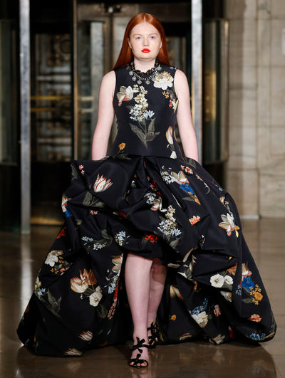 A model wears a black high low gown with flowers and vases printed