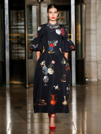 A model wears a black dress with printed flowers and vases