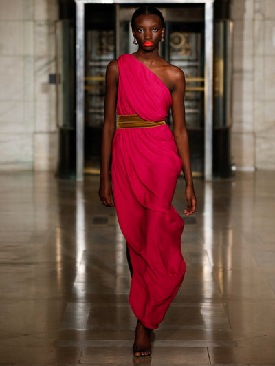 A model wears a one shoulder pink gown with a velvet green belt