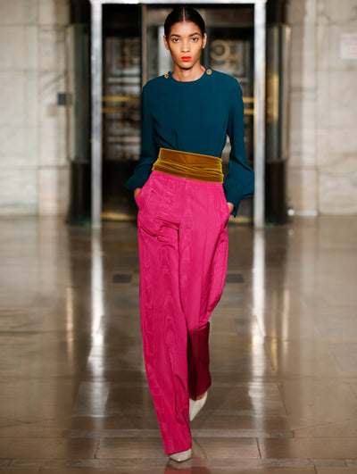 A model wears pink pants with a velvet green belt and navy top