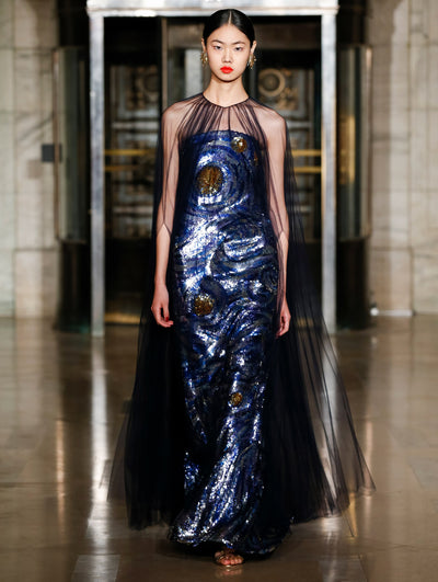 A model wears a blue dress with a black see-thru cape