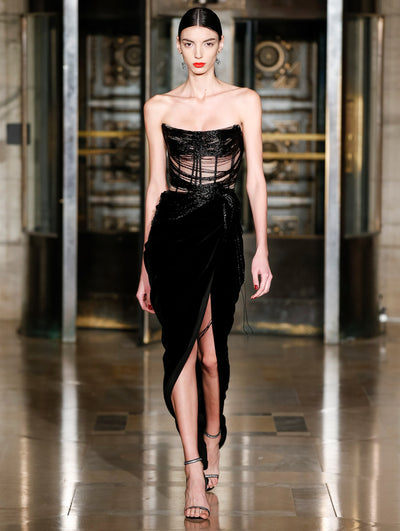 A model wears a black dress with velvet on the bottom and a slit