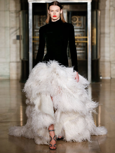 A model wears a gown with black long sleeves/top and ruffle white feathers for the skirt
