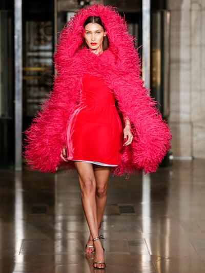 A model wears a red cocktail dress with pink cape