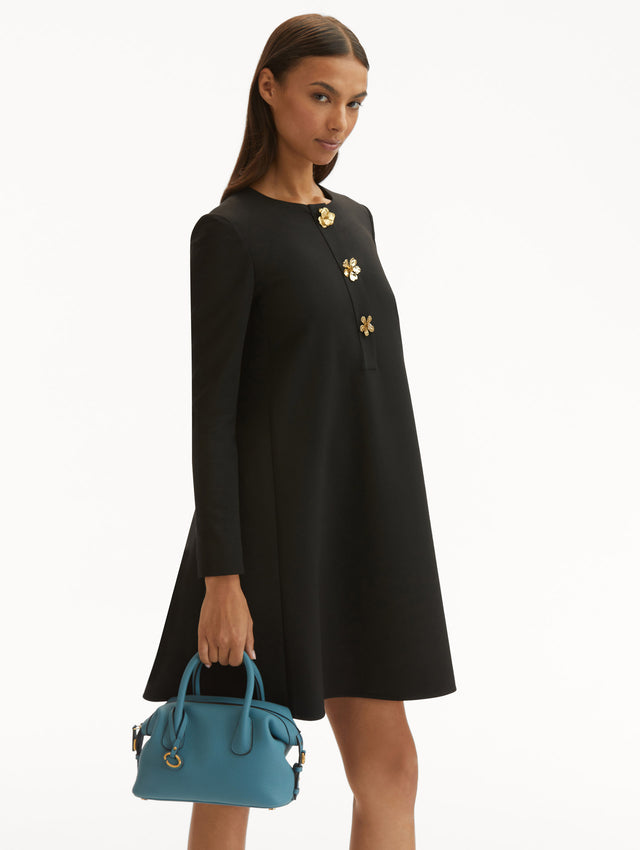 Model in black dress holding The Mini Dahlia leather handbag in blue with O logo around the handle. Front View