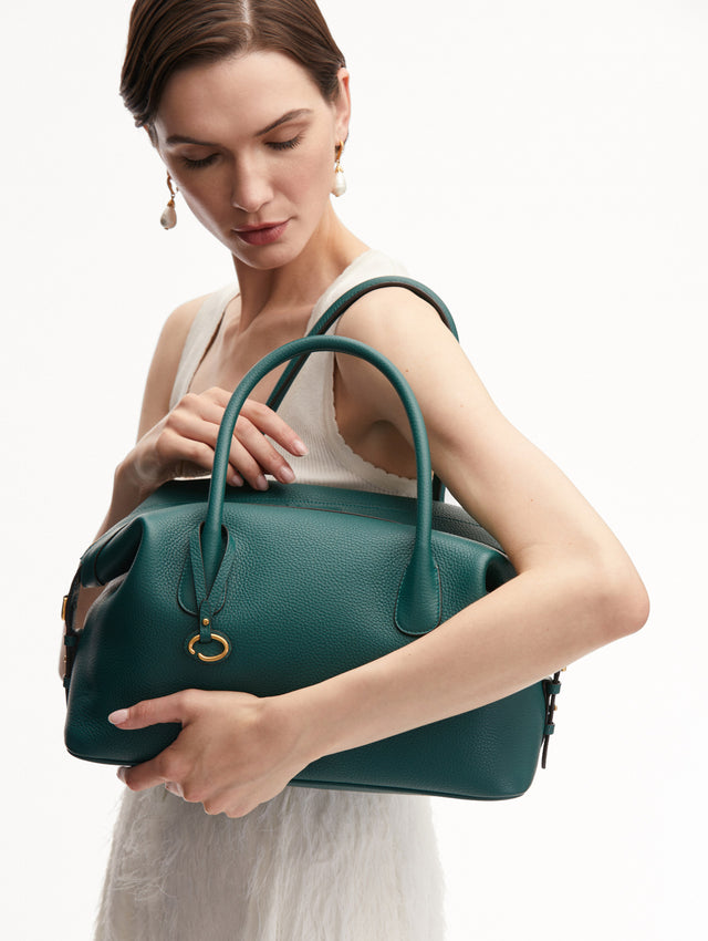Model Holding the Dahlia Leather Handbag in Green with Detachable Shoulder Strap and O logo tag around the Top Handle.  Front View