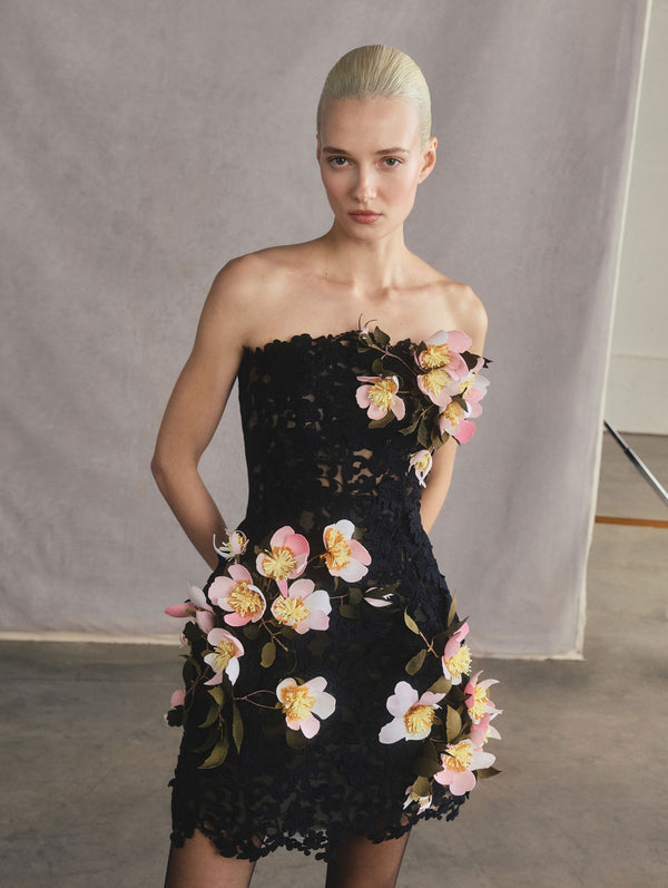 The model is wearing a black, lace, sleeveless dress with floral accents.