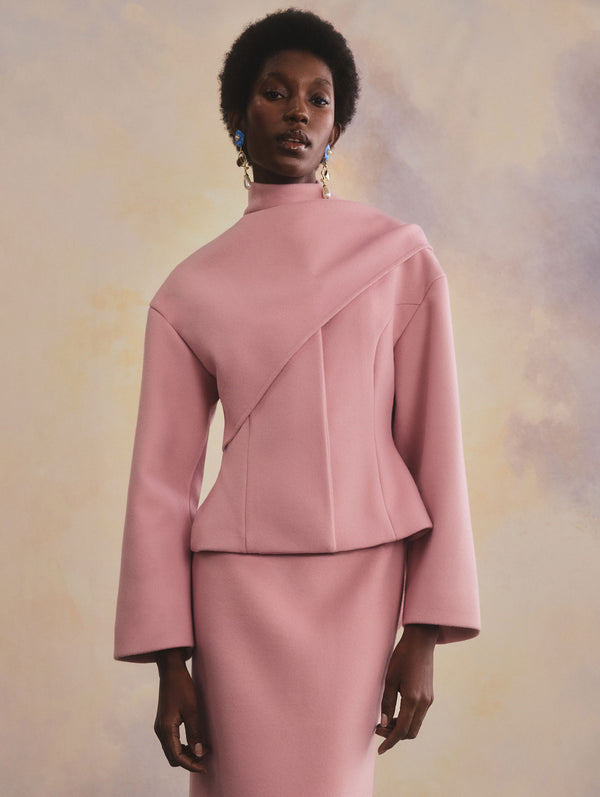 The model is wearing a pink long-sleeve blouse and skirt set.