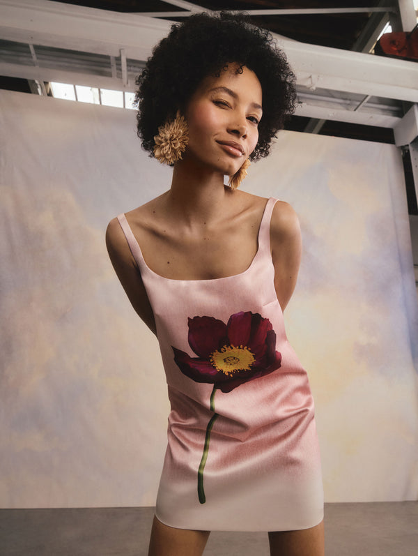 The model is wearing a pink mini dress with a poppy flower detail.