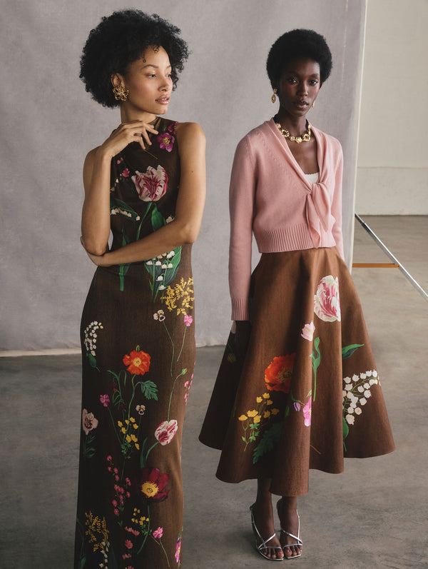 The two models are posed standing side-by-side. The model on the right is wearing a brown dress with floral detailing. The model on the right is wearing a pink cardigan and a brown skirt with floral detailing.