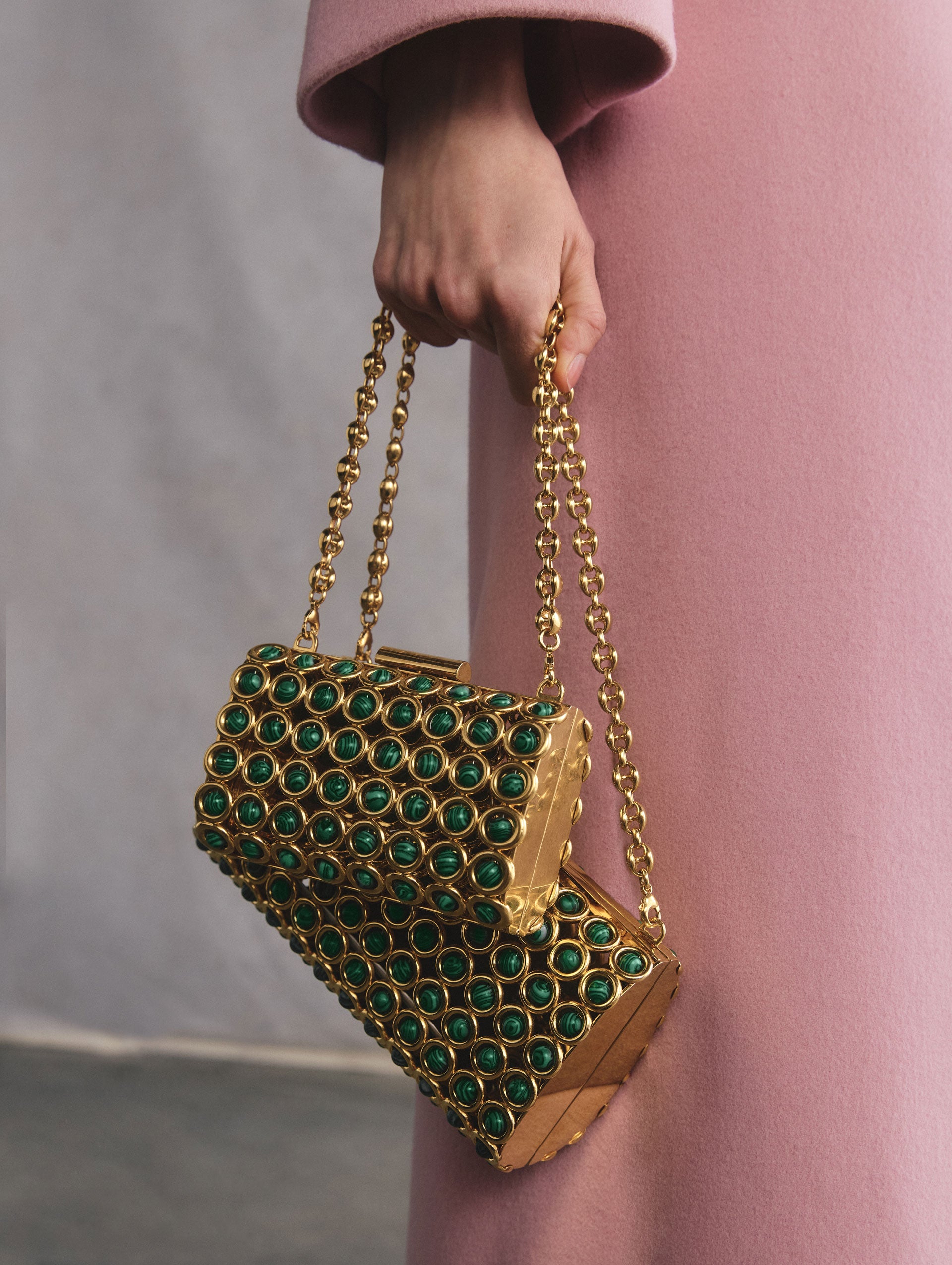 The model is holding two gold-toned bags featuring malachite stones.