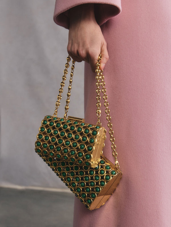 The model is holding two gold-toned bags featuring malachite stones.