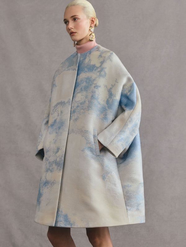 The model is wearing a coat that features a sky, cloud design.