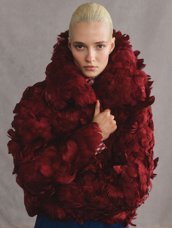 The model is wearing a wine-red feather, short coat.