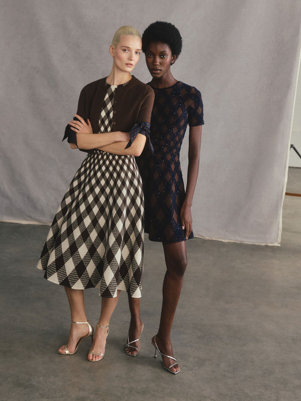 The two models are posed standing beside each other. The model on the left is wearing a black and white argyle midi dress and an argyle tie knit cardigan. The model on the right is wearing a beaded argyle fit & flare mini dress.