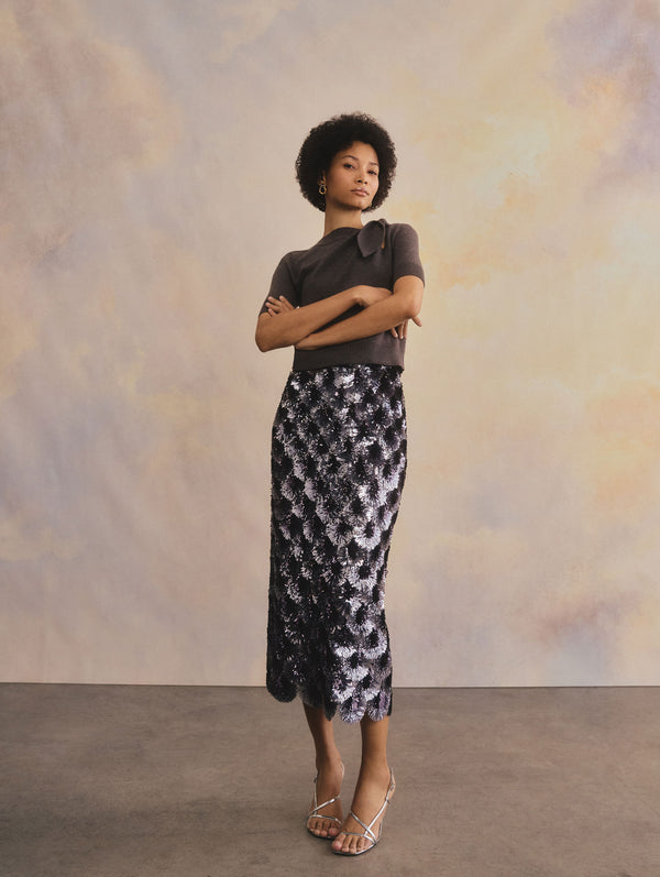 The model is wearing a scalloped embroidered pencil skirt and a tie neck short sleeve knit top.