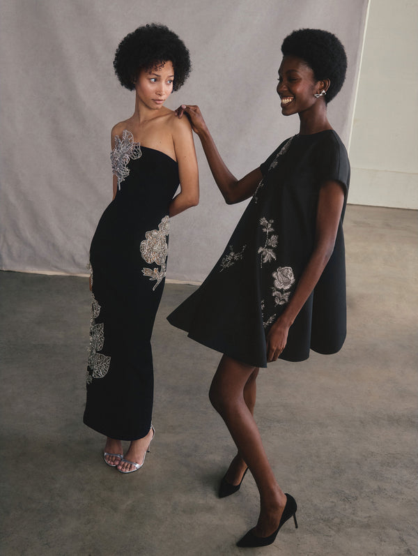 The two models are posed beside each other with one's hand on the other's shoulder. The model on the left is wearing a strapless crystal eaten leaves wool cocktail dress. The model on the right is wearing a short sleeve flower applique wool shift dress.