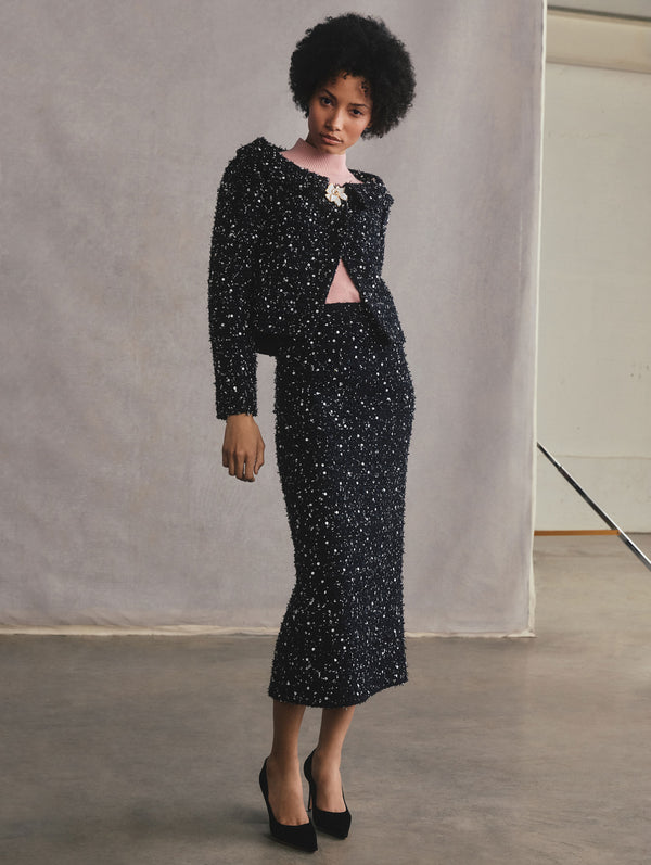 The model is wearing an off-the-shoulder sequin ribbon tweed jacket and a sequin ribbon tweed pencil skirt.