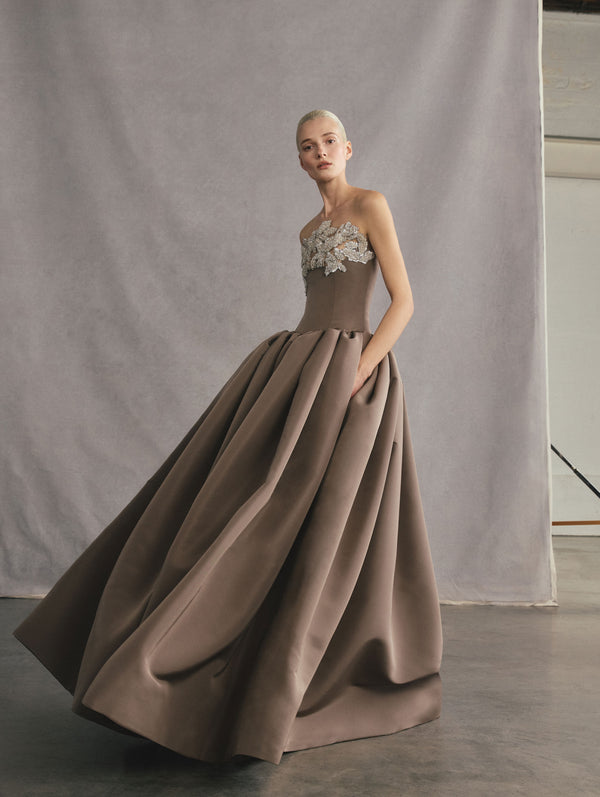 The model is wearing a strapless stone-grey colored ball gown with silver rhinestone embroidery at the neckline.