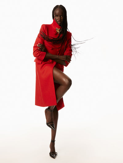 Model wearing buttoned up red jacket with a gold accent around on the neck. 