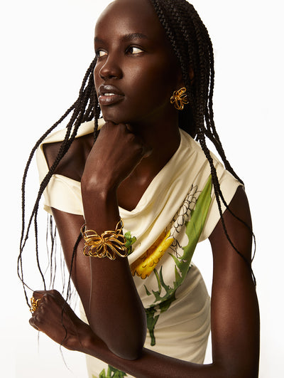 Model is wearing ivory dress with printed florals, model wearing a floral gold wire bracelet and gold floral bracelet. 