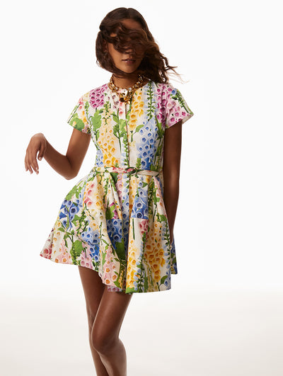 Model is wearing short sleeve white dress with printed pink, blue, yellow and green foxgloves with a matching self-belt. 