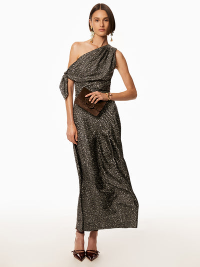 Model wearing one shoulder black silk twill dress and holding a brown suede hang bag and wearing drop pearl earrings. 